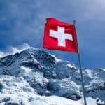 A swiss flag in front of a snow covered mountain